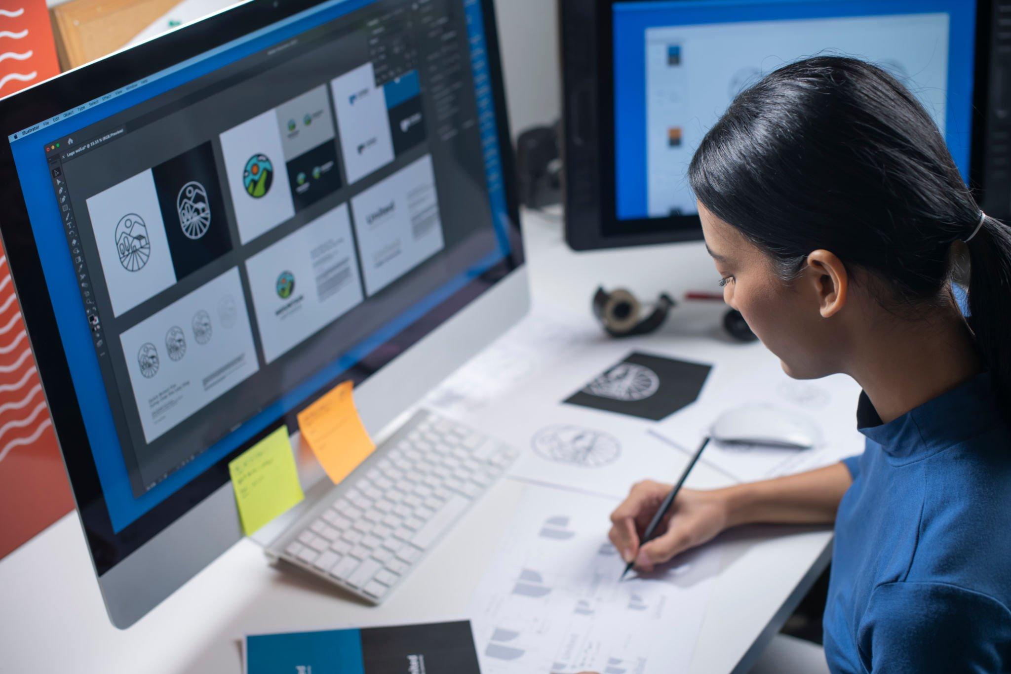 Woman developing branding guidelines and logo design on her computer and on paper.